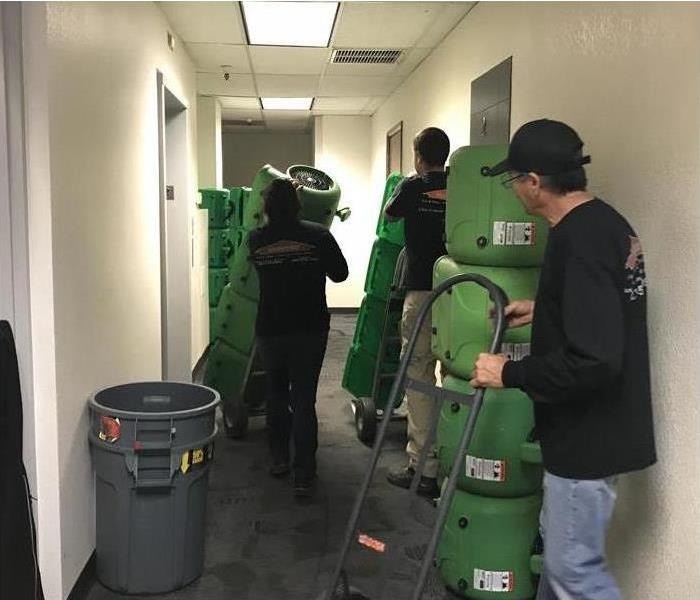 Three technicians introducing air movers in a building for drying purposes after water damage